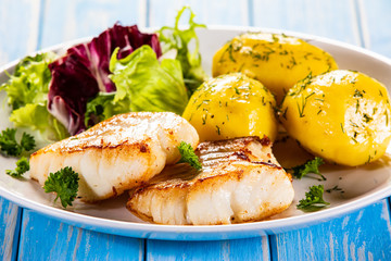 Fish dish - fried cod fillet with potatoes and vegetables on wooden table
