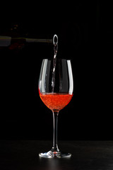 Rose wine pouring in a glass on black background