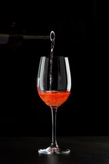 Rose wine pouring in a glass on black background