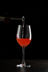 Rose wine pouring in a glass on black background