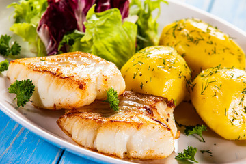 Fish dish - fried cod fillet with potatoes and vegetables on wooden table
