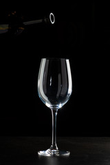 Red wine pouring into a glass with drops on black background