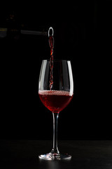 Naklejka na ściany i meble Red wine pouring into a glass with drops on black background