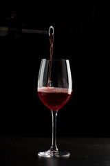 Red wine pouring into a glass with drops on black background
