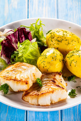 Fish dish - fried cod fillet with potatoes and vegetables on wooden table
