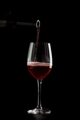 Red wine pouring into a glass with drops on black background