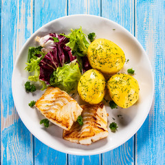 Fish dish - fried cod fillet with potatoes and vegetables on wooden table
