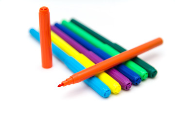 Colorful markers lying in a row on a white background. Opened orange marker lies on top of the other ones. Art and education.