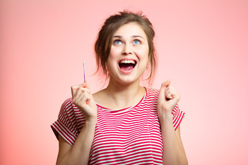 young happy woman with positive result result of pregnancy test, excited future mother with mouth opened, family planning, motherhood concept on pink studio background
