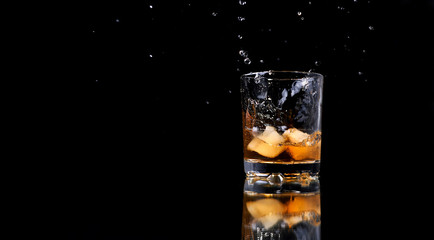glass of whiskey with ice and a splash on a black background