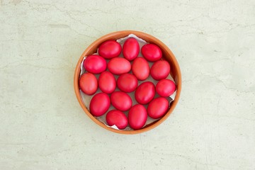 Isolated on a white marble table, homemade painted red hard boiled eggs in a ceramic round bowl for Easter Sunday holidays. Top view