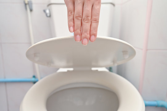 Cropped hand of yoman is holding toilet lid by caution. Avoid virus and unhygiene concept.