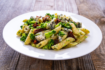 Penne with gorgonzola broccoli and sun-dried tomatoes on wooden table