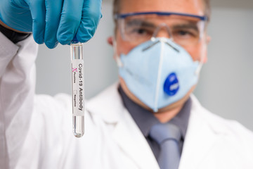 Scientist or doctor with medical face mask and medical gloves is handling virus test tube with...