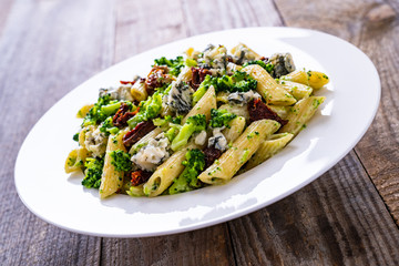 Penne with gorgonzola broccoli and sun-dried tomatoes on wooden table