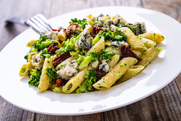 Penne with gorgonzola broccoli and sun-dried tomatoes on wooden table