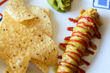 Corn dog o salchicha rebozada con mostaza y ketchup acompañada de nachos con guacamole