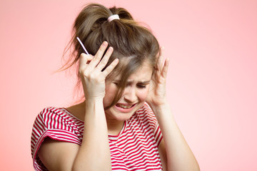 Anxious young woman with medical pregnancy test on pink studio background, disappointed girl cry in stress, concept of unplanned motherhood