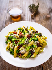 Penne with gorgonzola broccoli and sun-dried tomatoes on wooden table