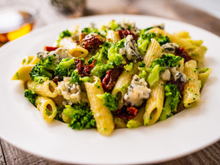 Penne with gorgonzola broccoli and sun-dried tomatoes on wooden table
