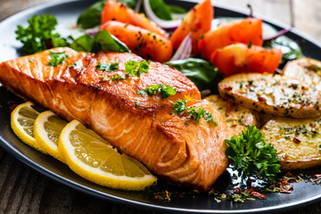 Fried salmon steak with potatoes and vegetables on wooden table