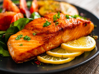 Fried salmon steak with potatoes and vegetables on wooden table