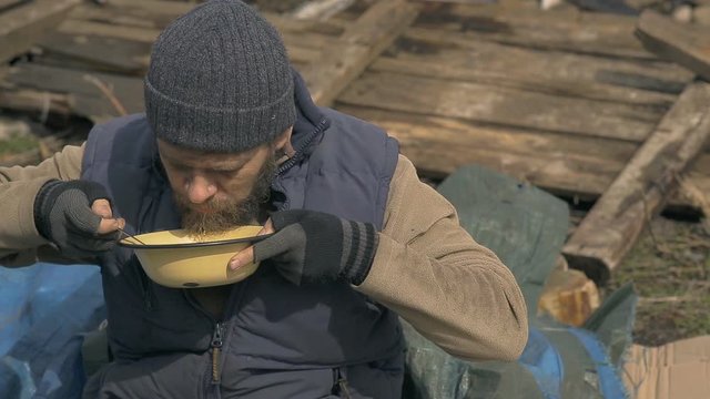 a homeless man eats soup from a plate near the ruins, helping poor and hungry people during the epidemic