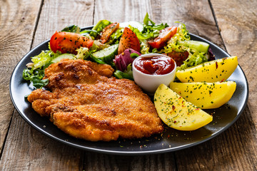 Pork chop with boiled potatoes and vegetable salad on wooden background
