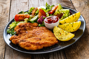 Pork chop with boiled potatoes and vegetable salad on wooden background
