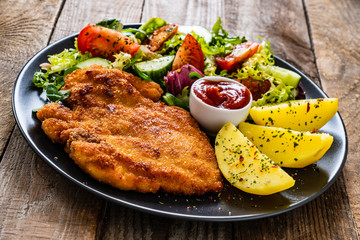 Pork chop with boiled potatoes and vegetable salad on wooden background
