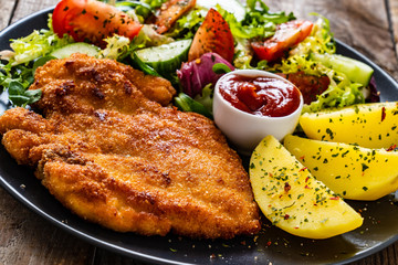 Pork chop with boiled potatoes and vegetable salad on wooden background
