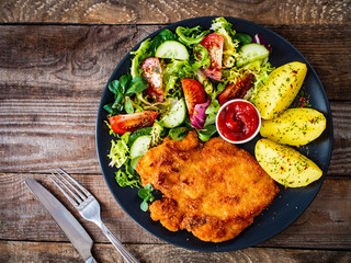 Pork chop with boiled potatoes and vegetable salad on wooden background
