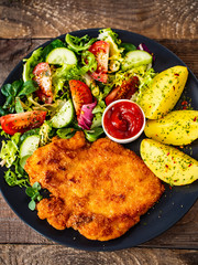Pork chop with boiled potatoes and vegetable salad on wooden background
