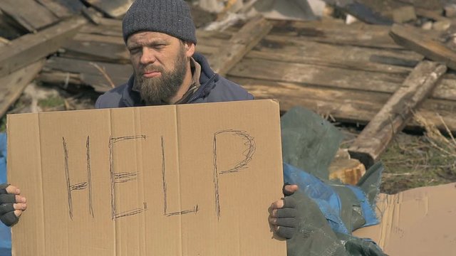 a homeless man near the ruins with a sign help, help the poor and hungry people during the epidemic