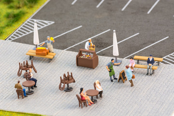 Social distancing rules with miniature people at a sidewalk cafe