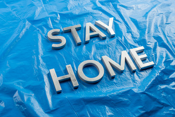 the words stay home laid with silver metal letters on crumpled blue plastic background in slanted...