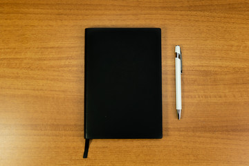 Stationery set with A5 paper notebook with black cover and white pen for mockup purposes in a wood background