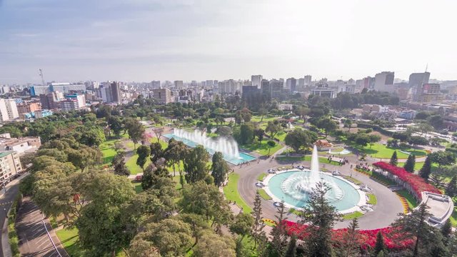 Aerial view to Park of the Reserve with magic water circuit biggest fountain complex timelapse. Green lawn and trees. City skyline on a background