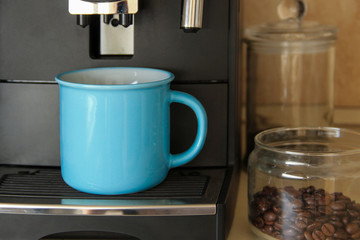 Blue coffee mug and coffee machine standing in the kitchen. Professional coffee blending machine.