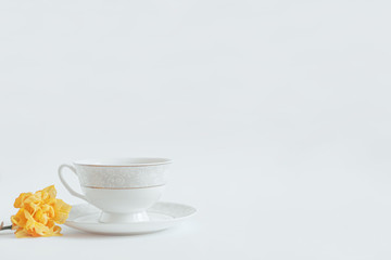 Cup of tea with a plate on a table with a flower on a white background