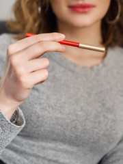 Woman's beauty blogger hands holding red cosmetic pencil with blurred body background, warm cozy tones and copyspace