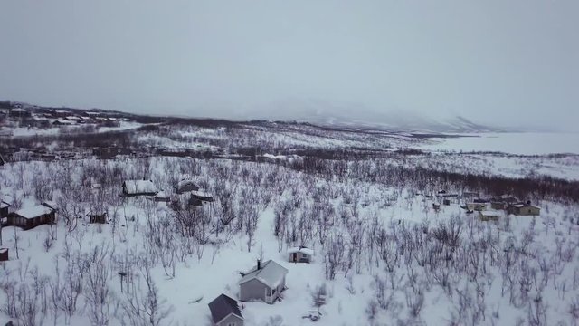 Wooden homes in the snow white landscape of Abisko Village in Sweden by the frozen lake - aerial