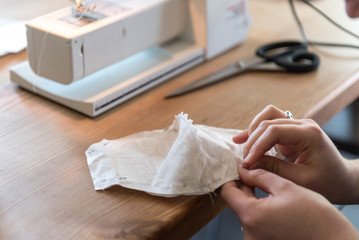 Do it yourself, woman hands using the sewing machine to sew a white face mask during the corona virus pandemia. Home made diy protective mask against virus. Selective Focus