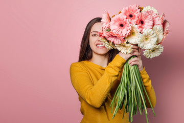Young woman dressed in yellow sweater with  bouquet of  gerberas on pink background