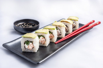 Sushi roll with avocado wrap, grilled salmon, philadelphia cheese and green onions Black container and red chopsticks