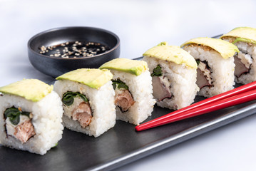 Sushi roll with avocado wrap, grilled salmon, philadelphia cheese and green onions Black container and red chopsticks