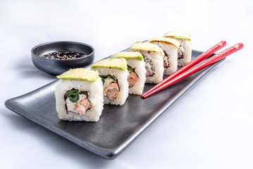 Sushi roll with avocado wrap, grilled salmon, philadelphia cheese and green onions Black container and red chopsticks