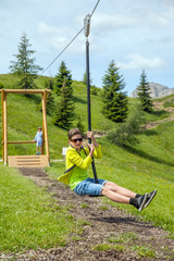 A thirteen years old boy is playing on playground in summer mountains, Italy