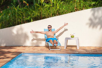 Happy man relaxing on sunbed close to swimming pool.
