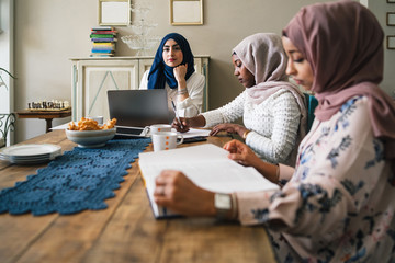Three young Muslim women study on books and laptop at the kitchen table - Arabian millennials are preparing for university exams